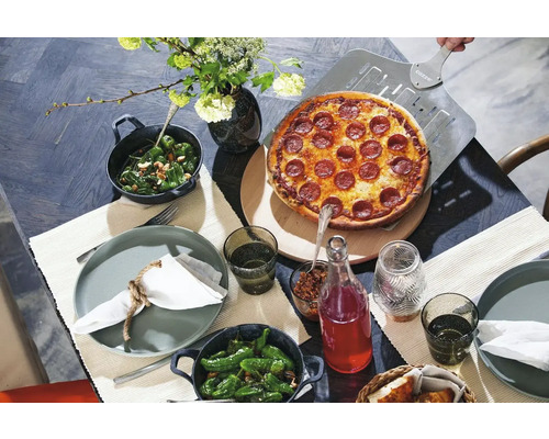 Eettafel gedekt met pizza, bijgerechten, borden, glazen en bloemen