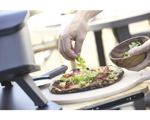 Pizza wordt belegd met rucola, pizzaoven en pizzaschep in beeld