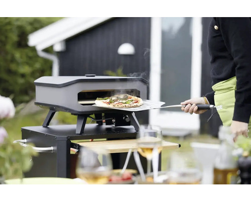 Pizzaoven met pizza op pizzaschep in de tuin