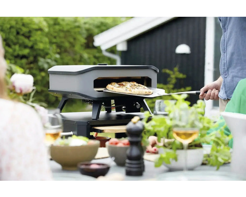 Pizzaoven in de tuin met persoon die pizza bereidt