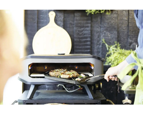 Buitengrill met kookruimte, waarin een gerecht wordt bereid, met een snijplank op de achtergrond