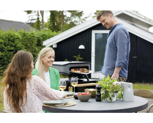 Buitenscène met draagbare pizzaoven, tafel en drie personen