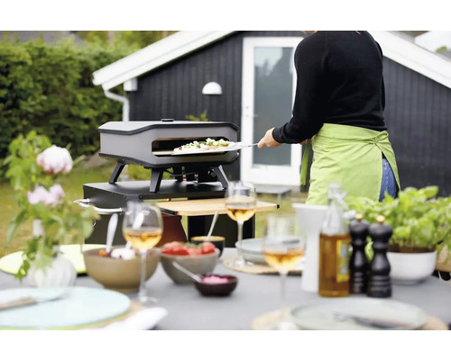 Buitenscène met pizzaoven, gedekte tafel en persoon die pizza maakt