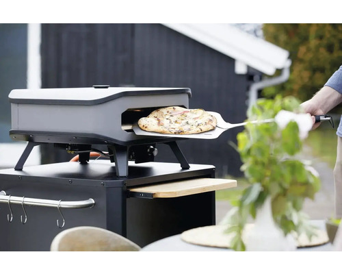 Pizzaoven met pizza op pizzaschep in de tuin