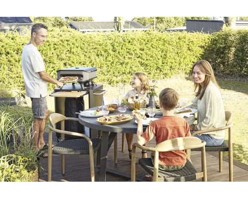 Buitenscène met familie, pizzaoven en eettafel op het terras.
