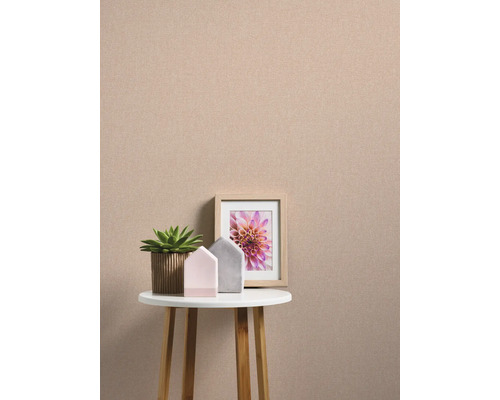 Decoratief stilleven met een plant, twee decoratieve huizen en een ingelijste afbeelding op een klein tafeltje voor een effen muur