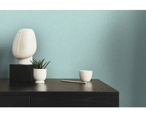 Licht, gestructureerd vliesbehang op een muur naast een dressoir met decoraties.