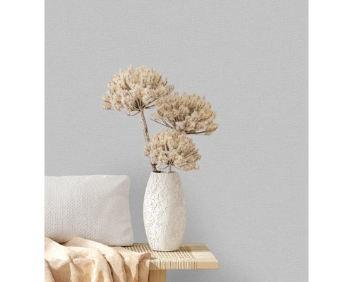 Decoratieve vaas met droogbloemen op een tafel met kussens tegen een gestructureerde wand