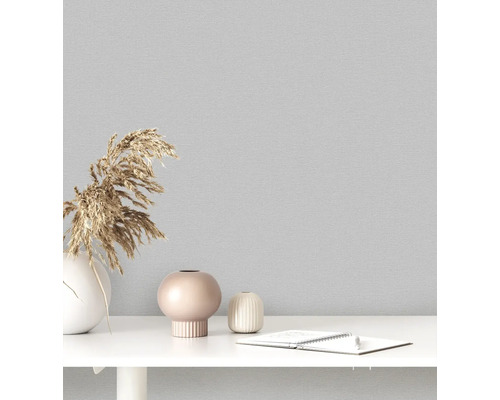 Close-up van een grijs textielbehang met decoratieve vazen en notitieblok op een tafel.