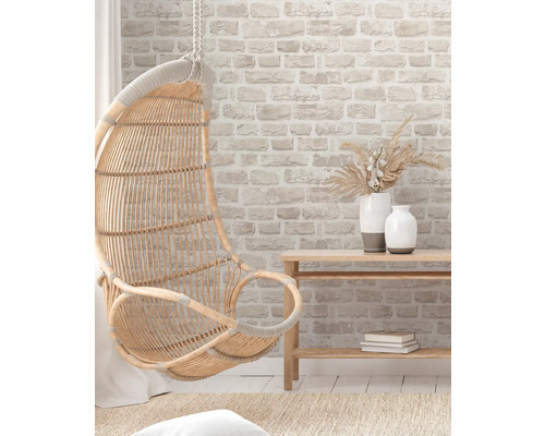 Scene met een hangende rotan stoel, een houten tafel en decoraties voor een bakstenen muur.