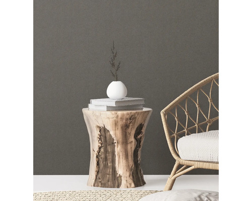 Decoratieve scène met een boomstronk als bijzettafel, met daarop boeken, een vaas en takken, naast een rotan stoel.