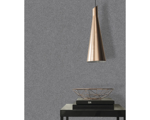 Close-up van een grijs behang met een fijne structuur in een kamer met een lamp en decoratieve objecten.