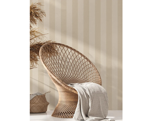 Decoratieve scène met rotan stoel, deken en mand tegen een gestreepte wand