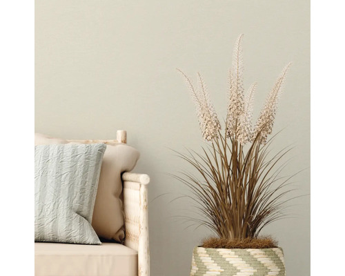 Decoratieve kunstplant in geweven mand naast een bank met kussens.