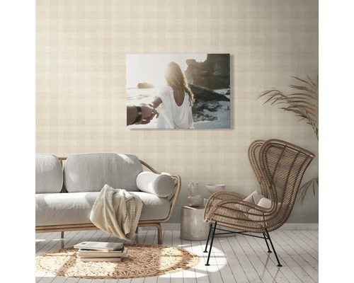 Woonkamer met bank, rotan stoel en muurfoto met strandmotief