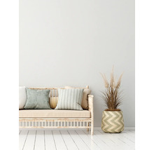 Decoratieve bank met kussens en een plant in een mand op een witte houten vloer.