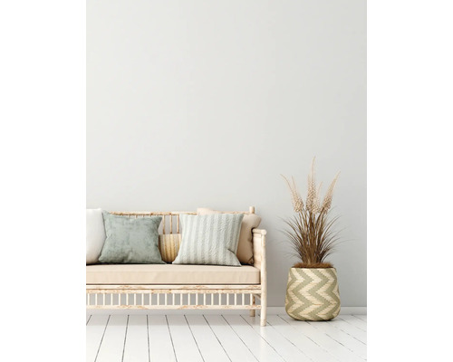 Decoratieve bank met kussens en een plant in een mand op een witte houten vloer.