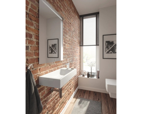 Badkamer met bakstenen muur, wastafel, spiegel en raam met jaloezieën.