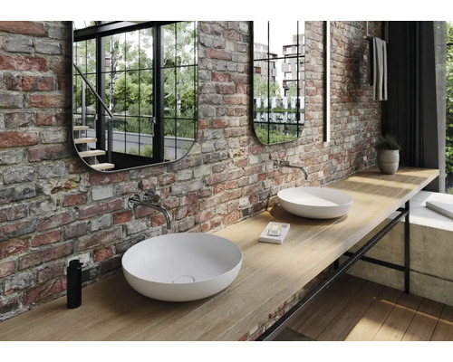 Badkamer met twee waskommen, twee spiegels en een muur van bakstenen.