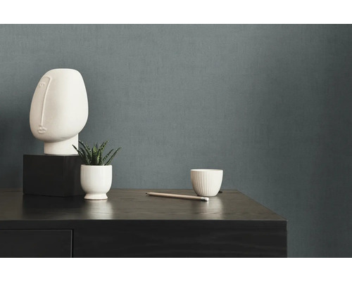 Decoratieve scène met sculptuur, plant en beker op een donkere houten commode voor een effen muur.