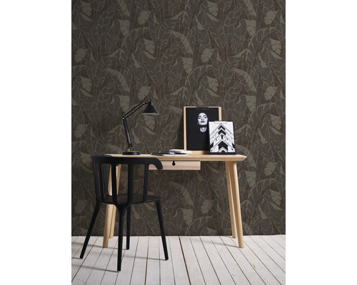 Decoratieve wand met bladerbehang achter een bureau met stoel.