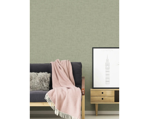 Woonkamer met een gestructureerd behang, een bank met een deken en kussens, en een klein kastje met een Londen foto