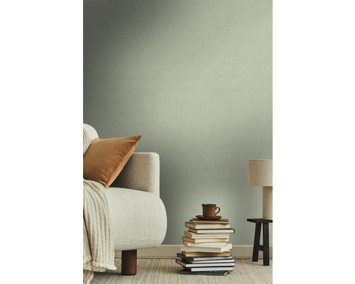 Woonkamer met textielbehang, bank, kussen, deken, stapel boeken, kop en lamp op een krukje