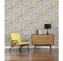 Woonkamer met fauteuil, commode, lamp, boeken en een behang met bloemmotief.