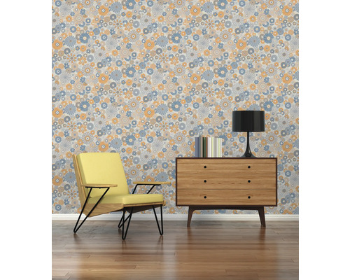 Woonkamer met fauteuil, commode, lamp, boeken en een behang met bloemmotief.