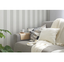 Woonkamer met gestreept behang, bank met kussens en deken en een dienblad met beker.