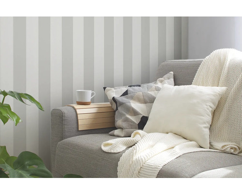 Woonkamer met gestreept behang, bank met kussens en deken en een dienblad met beker.