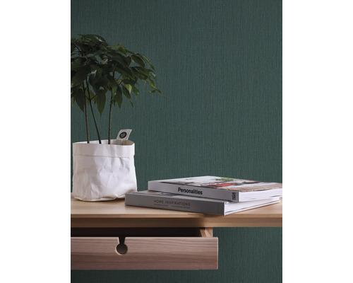 Close-up van een kamer met groen behang, een houten tafel, boeken en een kamerplant.