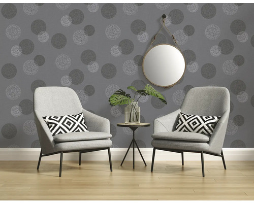 Twee fauteuils en een tafel met plant voor een muur met stippenbehang en een spiegel.