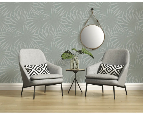 Kameroverzicht met twee grijze fauteuils, kleine tafel met plant, ronde spiegel en behang met palmmotief