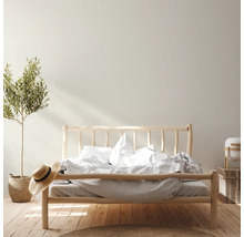 Lichte slaapkamer met houten bed, plant in mand en strohoed voor een vriendelijke sfeer.