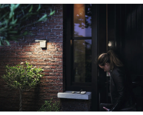 Een buitenwandlamp verlicht een huisentree met een bakstenen muur