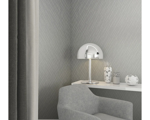 Scène met een grijs ruitjesbehang, een zilveren lamp, decoratieartikelen en een grijze fauteuil