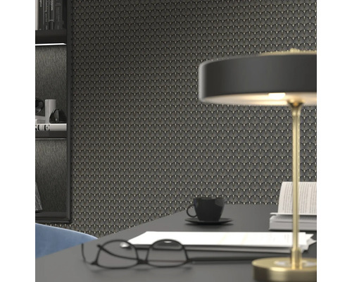 Close-up van een muur met art-decobehang, aangevuld met een bureau met een lamp, bril, koffiekopje en boeken.