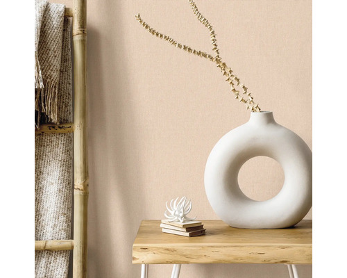 Woonkamer scène met bamboe ladder, textiel en decoraties zoals een witte donutvaas en een stapel boeken op een houten tafel tegen een effen muur.