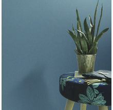 Decoratieve kamerplant in een versierde plantenbak op een kruk voor een wand.