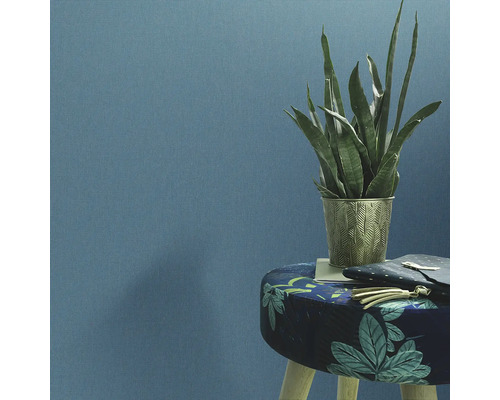 Decoratieve kamerplant in een versierde plantenbak op een kruk voor een wand.