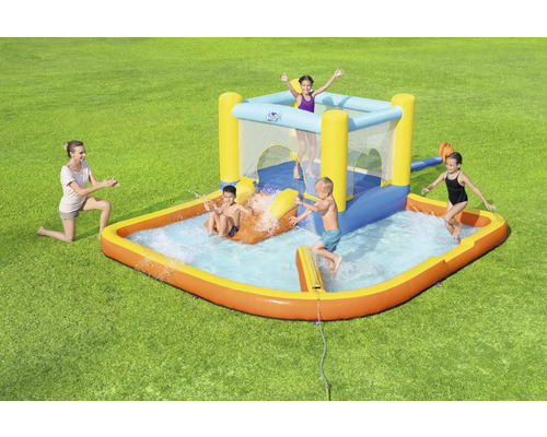 Opblaasbaar kinderzwembad met glijbaan en springkasteel op een groen gazon met spelende kinderen en een vrouw.