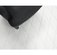 Detailopname van een fauteuil met een stoffen bekleding en een vloerkleed met ruitpatroon
