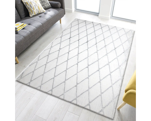 Wit vloerkleed met ruitpatroon op een lichte houten vloer, met een bank en fauteuil op de achtergrond.