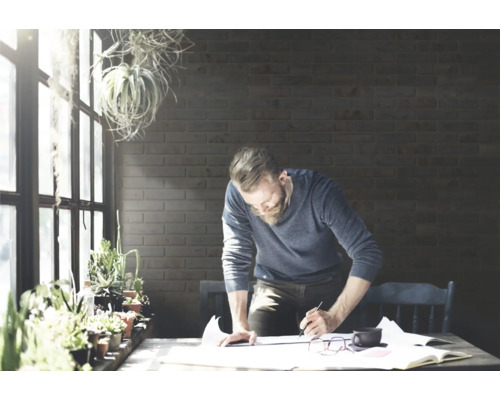 Man met baard werkt aan project aan tafel met planten en documenten.