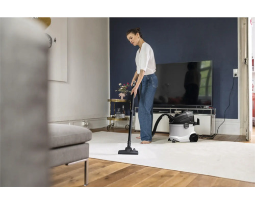 Vrouw stofzuigt met een alleszuiger een tapijt in een woonkamer