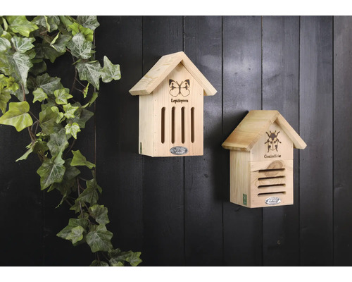 Twee houten insectenhotels hangen aan een muur met klimopbegroeiing.