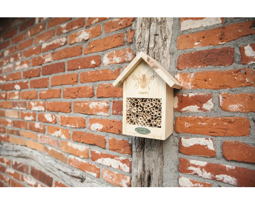 Insectenhotel van hout met bamboe buizen aan een bakstenen muur