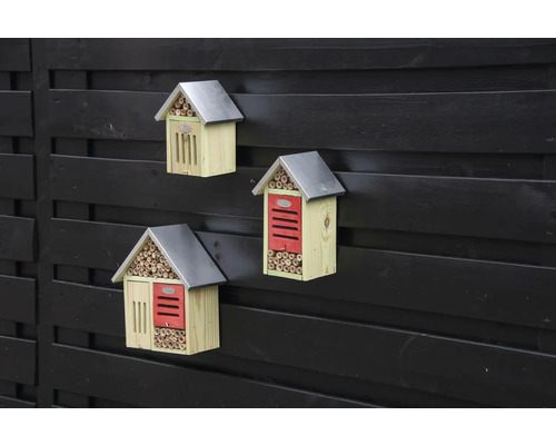 Drie houten insectenhotels met metalen dak aan een schutting