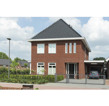 Aanzicht van een woonhuis met bakstenen gevel, donker dak en aangrenzende carport.